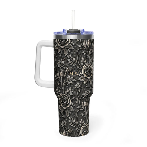 A tall handled tumbler with a black and gray floral rose pattern, featuring gold monogram initials 'M|W' on the front, a white handle, and a clear straw with a blue rim, shown on a white background.