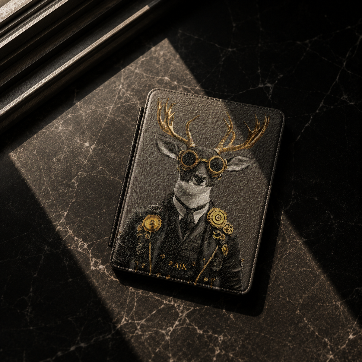 A dark-grey kindle case featuring a steampunk deer illustration with gold goggles, set on a dark marble surface with dramatic shadows.