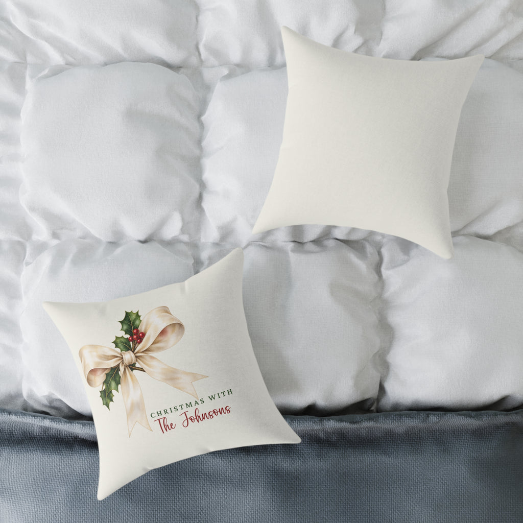 Front and back of the personalized cream bow and holly family name Christmas pillow on a white bed