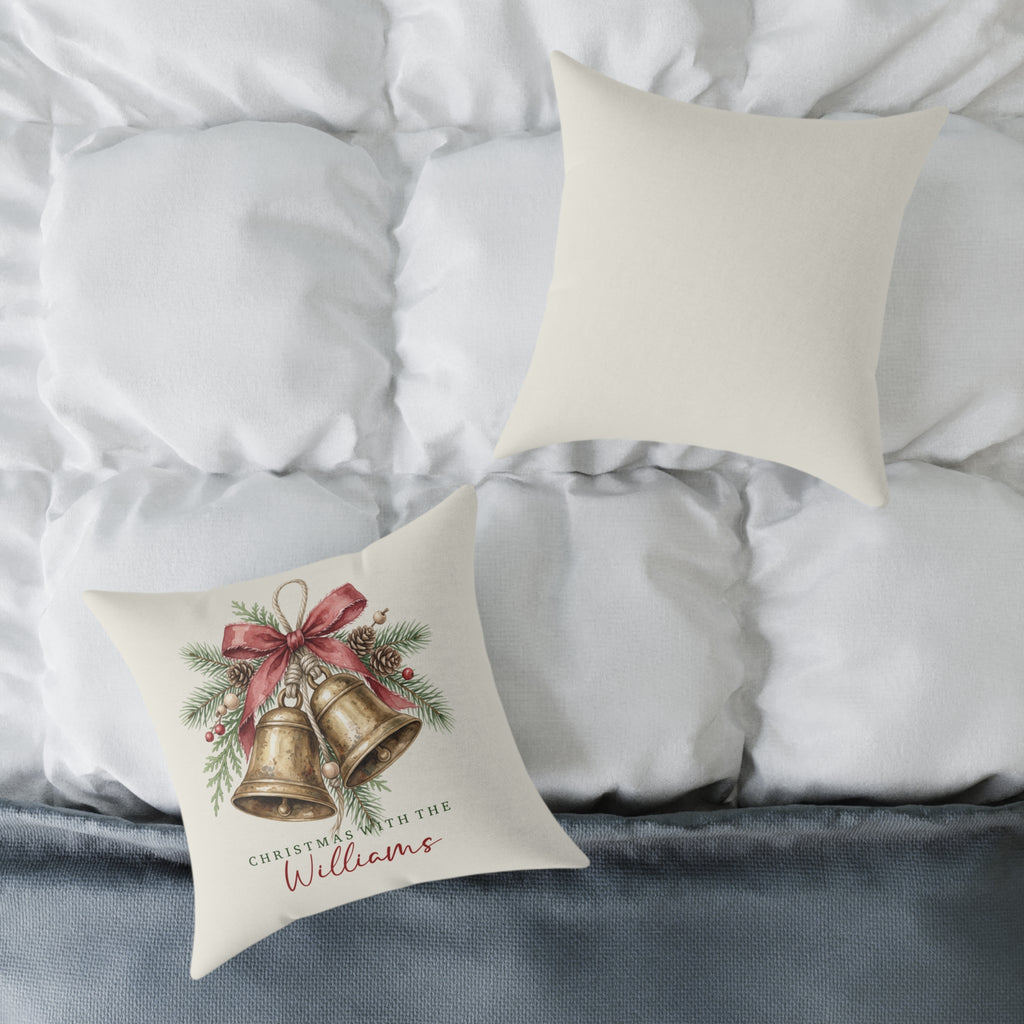 Front and back of the personalized brass bells family name Christmas pillow on a white bed