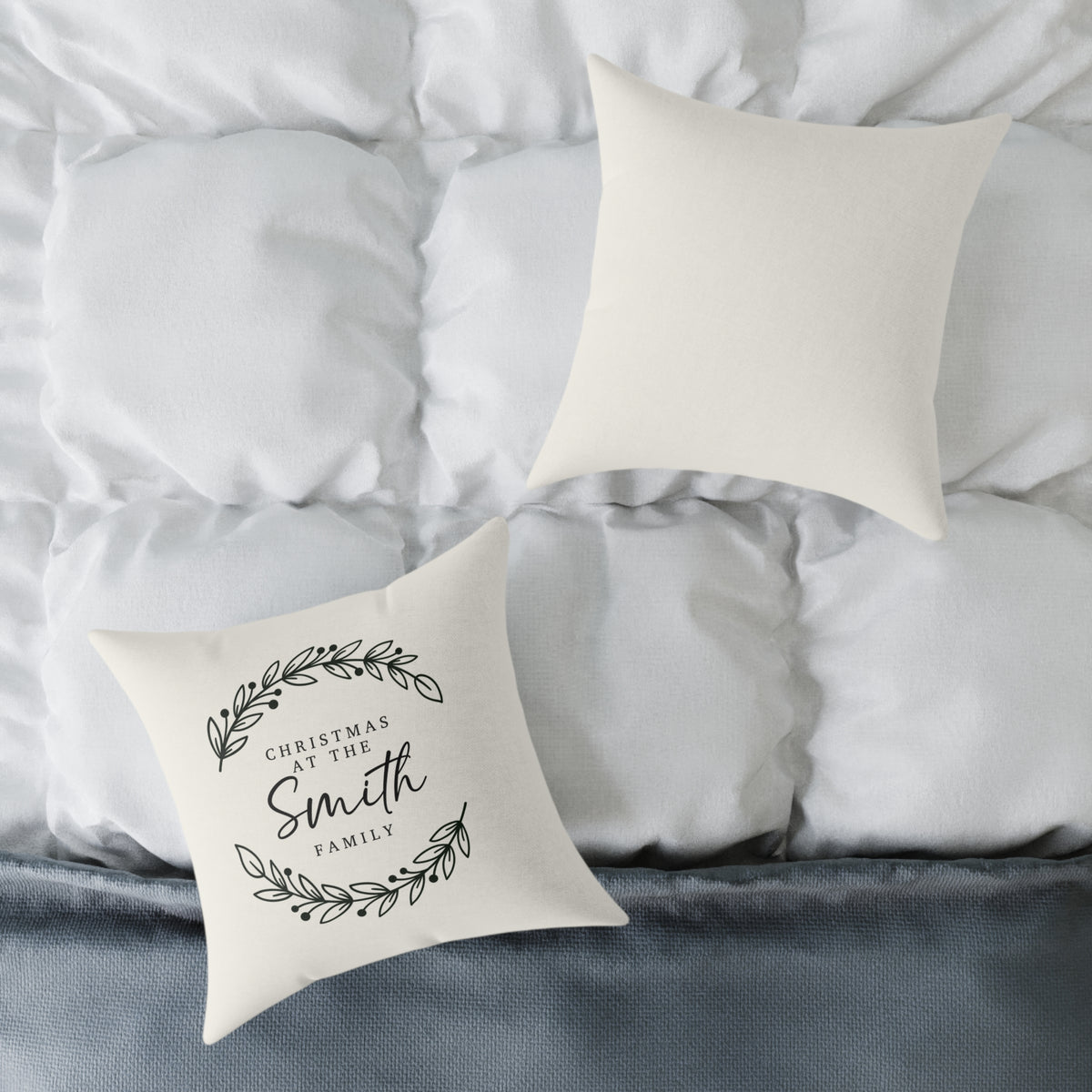 Front and back of the personalized laurel branches family name Christmas pillow on a white bed