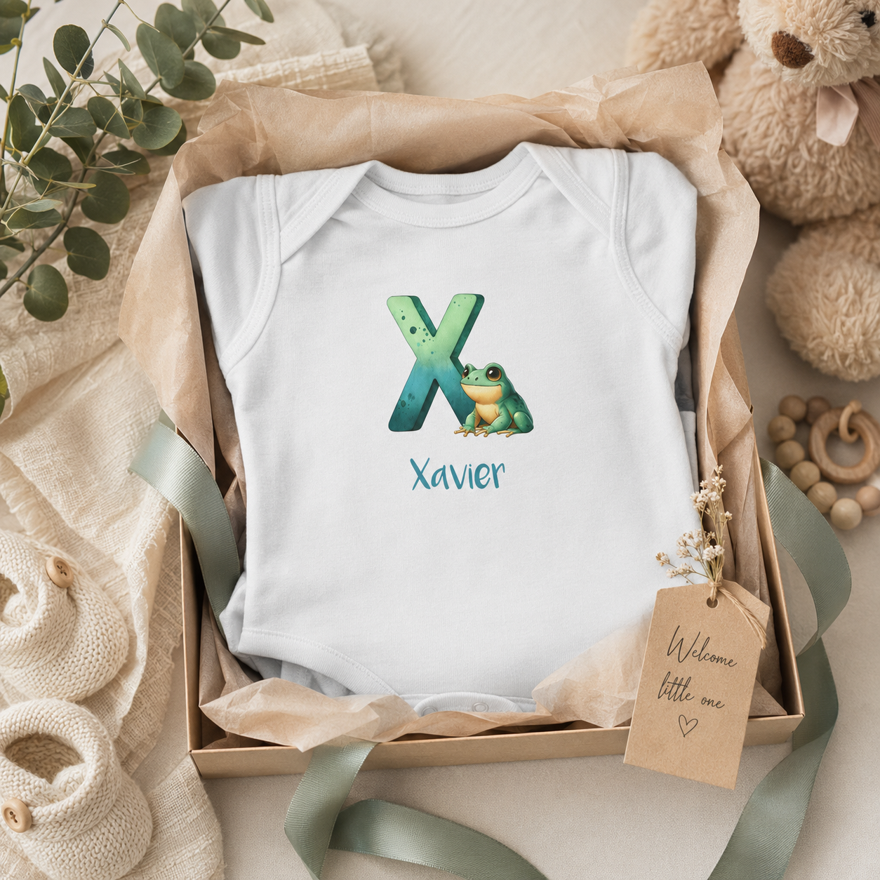 Close-up of X initial and frog on baby bodysuit